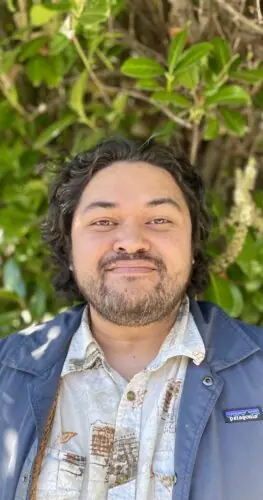 Dino Tenorio, AMFT therapist in Oakland, standing outdoors in front of greenery, smiling